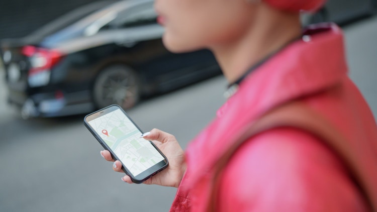 Una persona con giacca rossa consulta una mappa digitale con segnaposto su smartphone in strada.