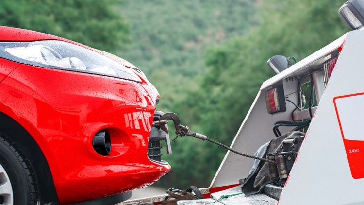 Primo piano di un gancio d&#39;acciaio che traina un&#39;auto rossa bagnata dalla pioggia sulla piattaforma di un carro attrezzi.
