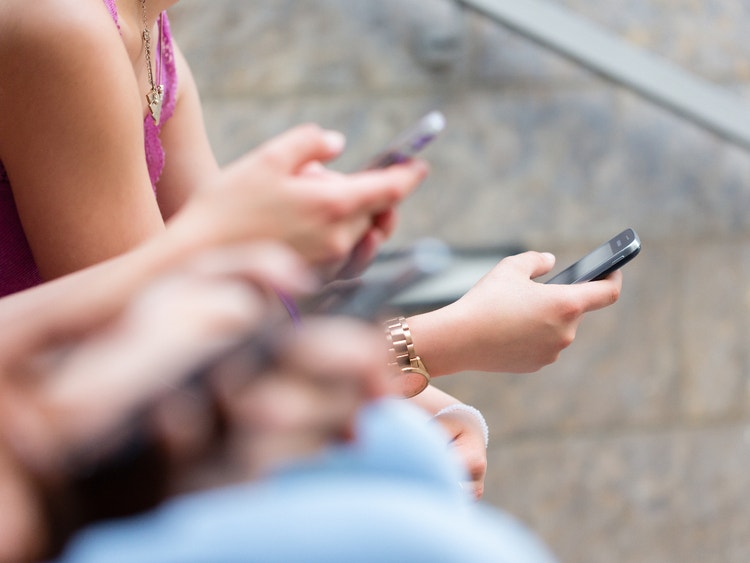 Dettaglio di diverse persone sedute all&#39;aperto che utilizzano i propri smartphone contemporaneamente.